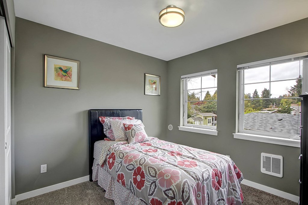 A bedroom with a bed, two windows, and two pictures on the wall.