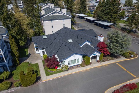 A white building with a grey roof is surrounded by trees and bushes.