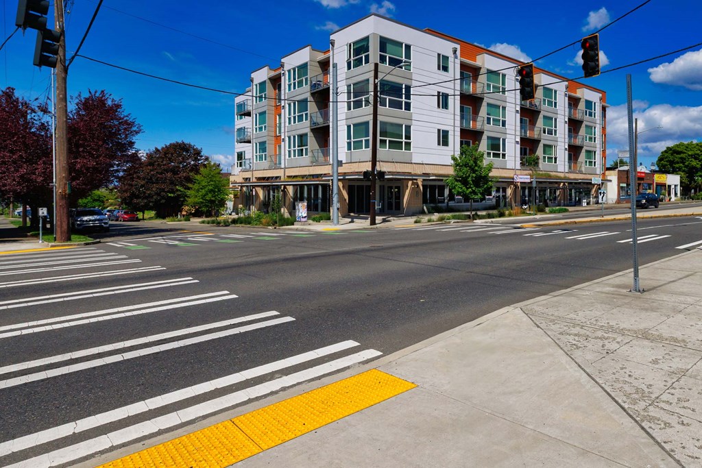 A multi-story building with a red and white facade is situated on a street corner with a crosswalk in front of it.