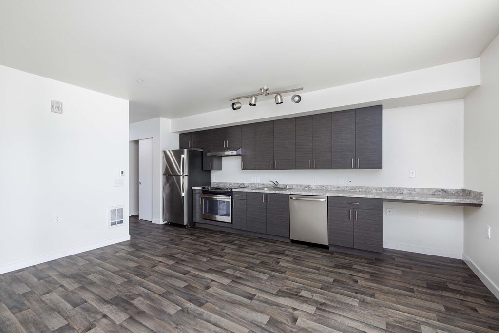 A kitchen with a white wall and a wooden floor.
