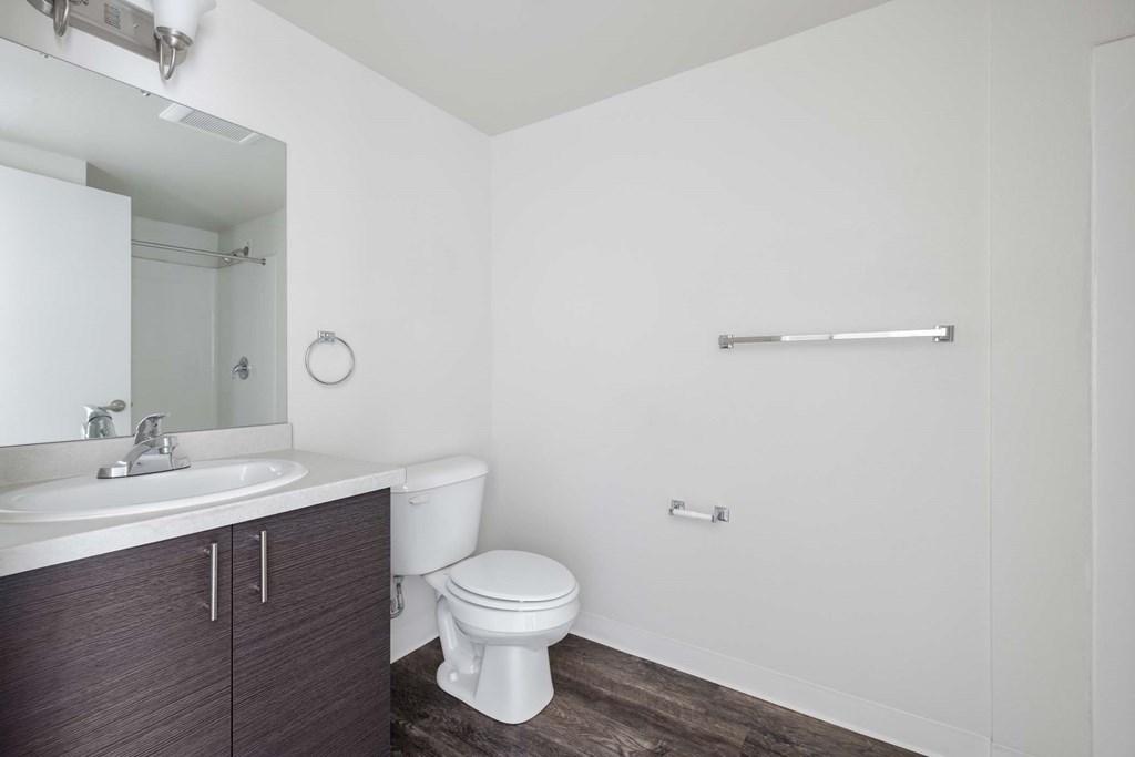 A white toilet sits in a bathroom with a wooden floor and a white sink.