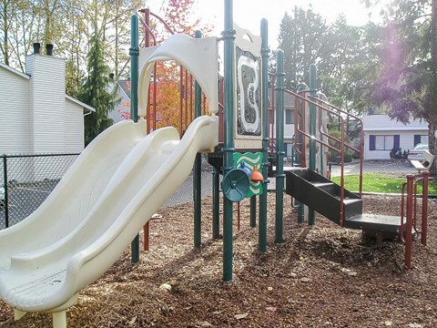 A playground with a slide, swings, and a seesaw.