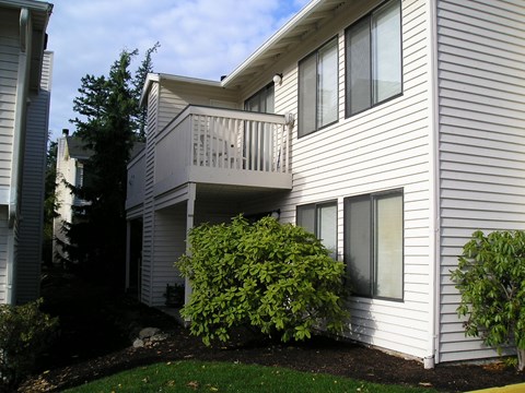 A white house with a balcony and bushes in front.