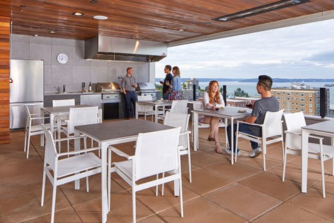A group of people are gathered around a table in a modern outdoor kitchen.
