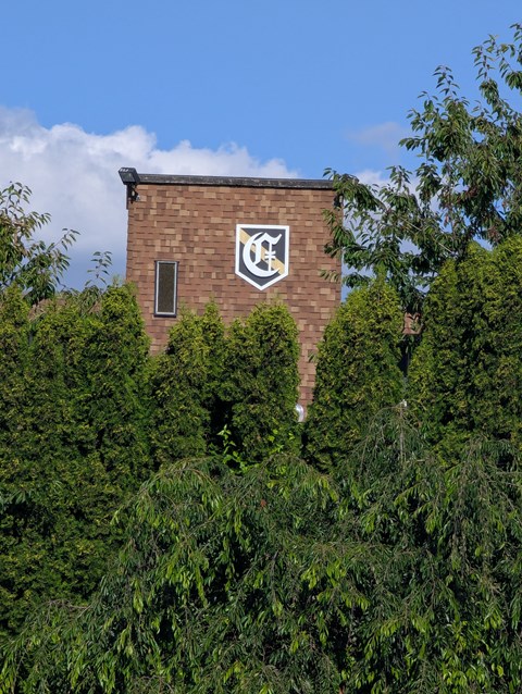 A building with a white emblem on a brick wall surrounded by greenery.
