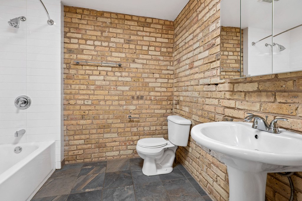 a bathroom with a toilet sink and shower and a brick wall
