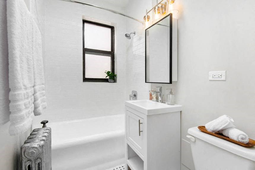 White bathroom with a shower tub, under sink storage mirror and toilet