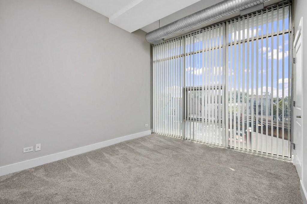 the living room has a large window with vertical blinds and carpeted flooring