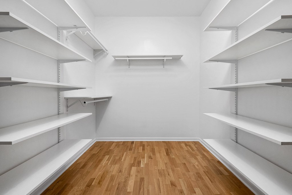 a walk in closet with white shelves and wood floors