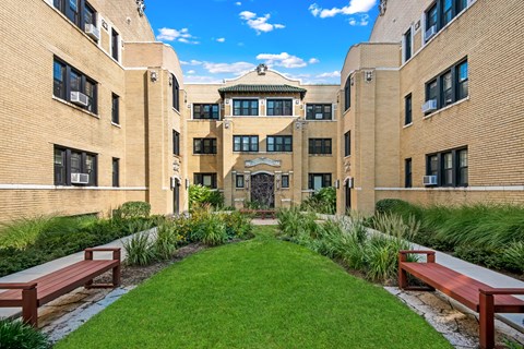 a courtyard between two buildings with benches and grass