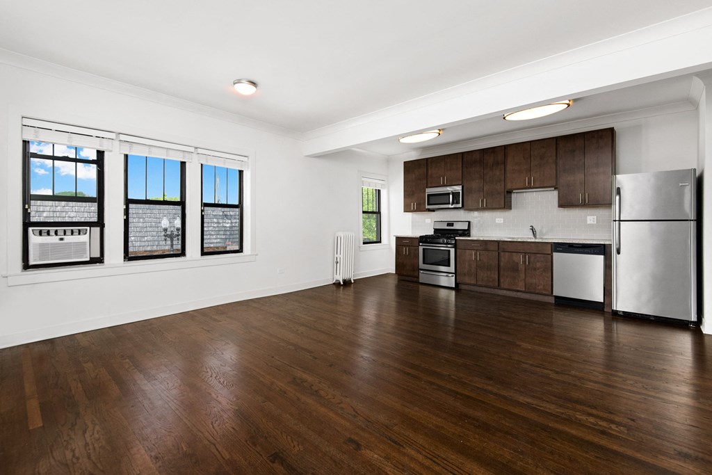 an empty kitchen and living room with wood flooring and stainless steel appliances