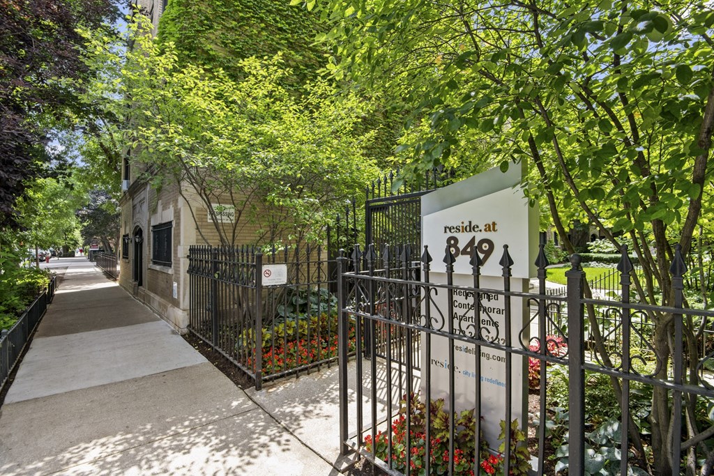 a sidewalk in front of a wrought iron gate with a sign on it