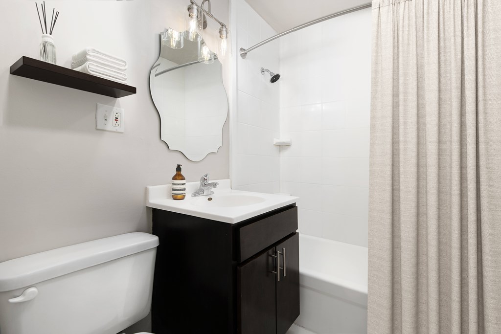 A white sink with a black cabinet and a white bathtub in a bathroom.