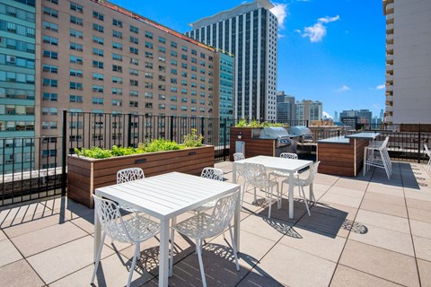 a rooftop patio with tables and chairs and a city in the background