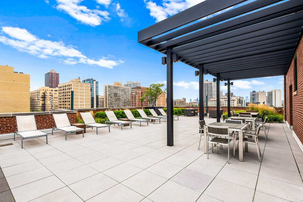 a rooftop patio with tables and chairs and a city in the background