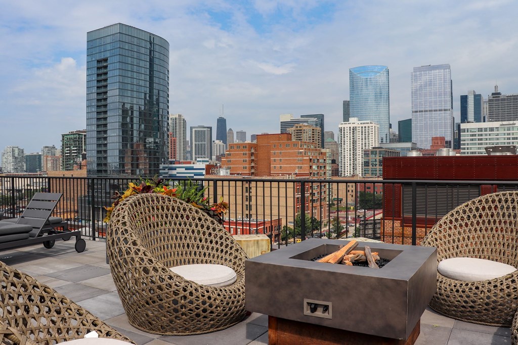 a rooftop patio with chairs and a fire pit overlooking the city