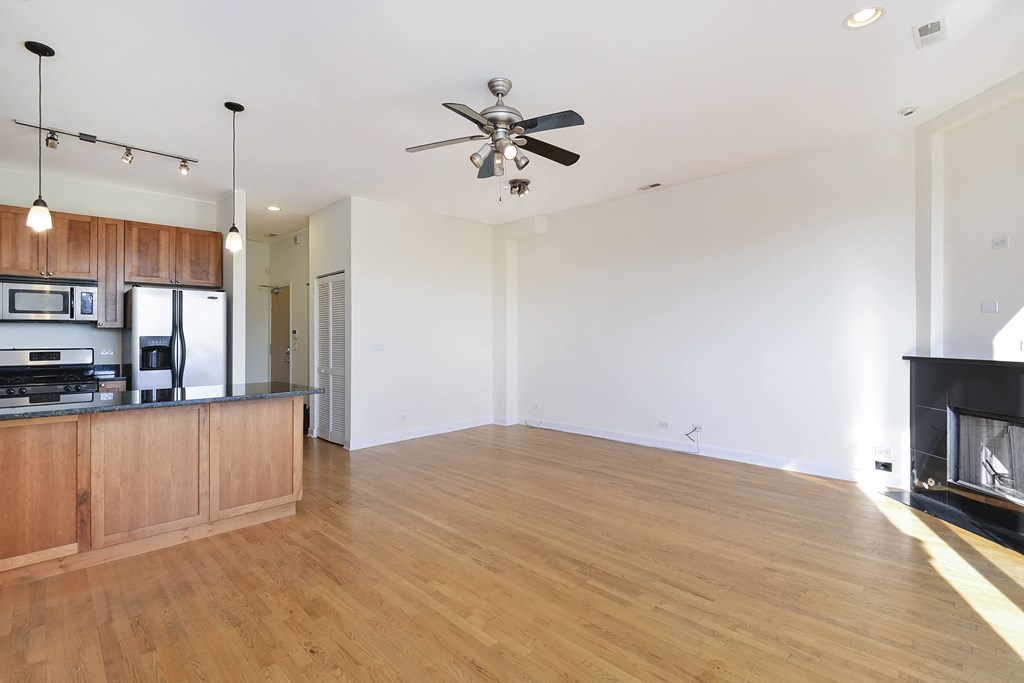 an empty living room with a ceiling fan and a kitchen