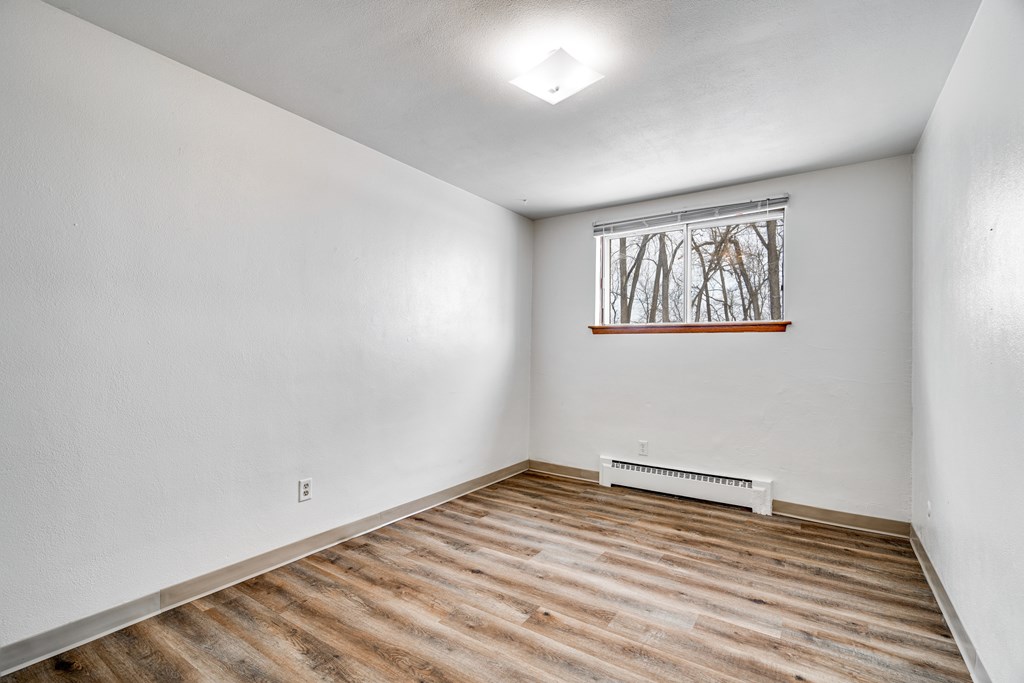 A room with wooden flooring and a window with a view of trees.