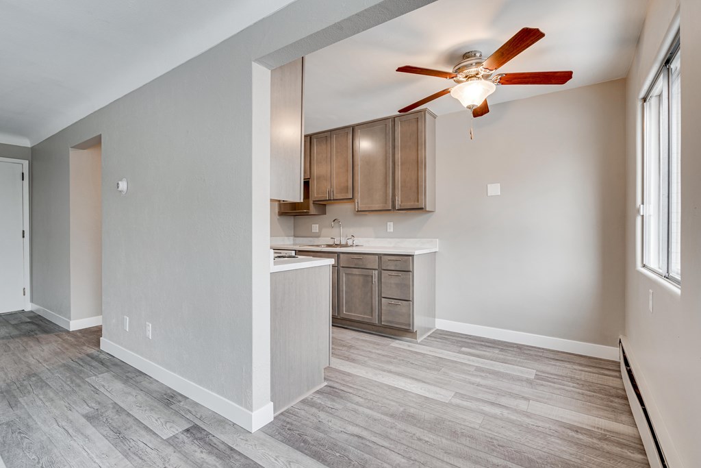 A room with a ceiling fan and a kitchen area in the background.