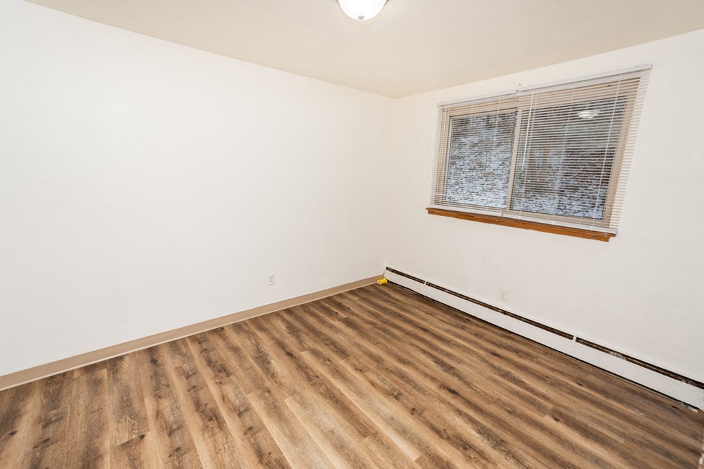 A room with wooden flooring and a window with blinds.