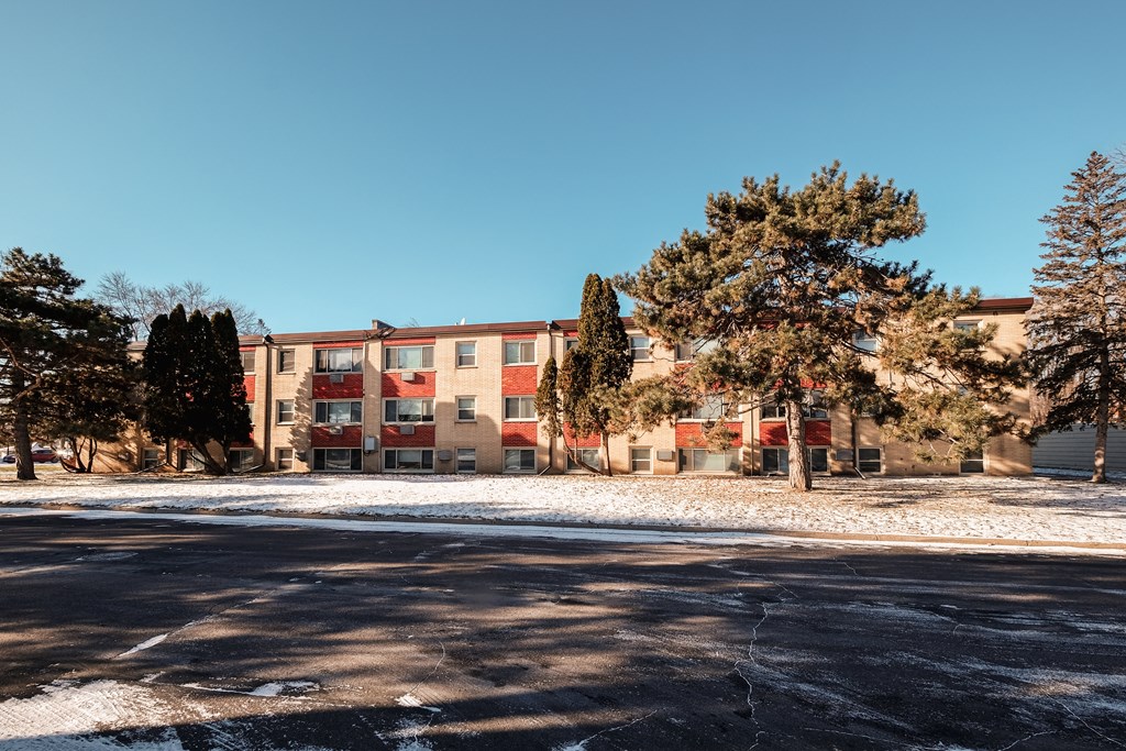 A building with a red and beige facade is surrounded by trees and snow.