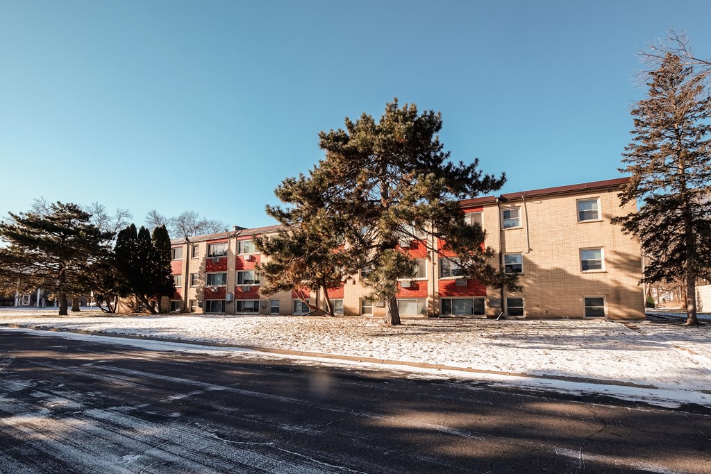 A snowy street with apartment buildings and trees.