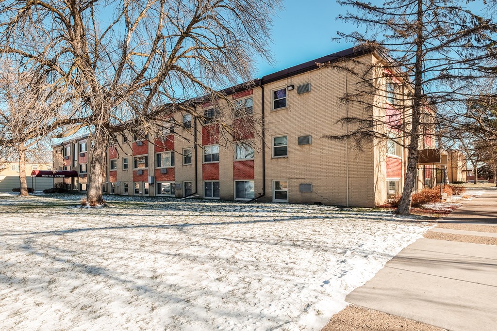 Apartment building with snow on the ground and bare trees in front.