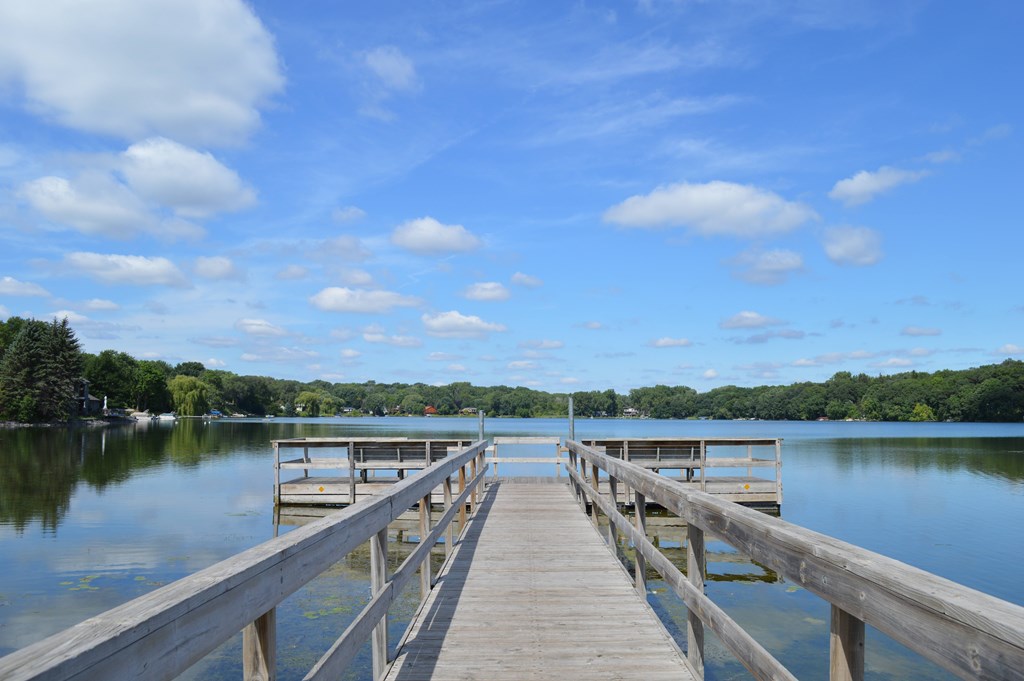 A wooden dock extends into a calm lake with a clear blue sky above.