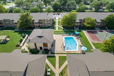 A swimming pool is surrounded by a grassy area and tennis court.