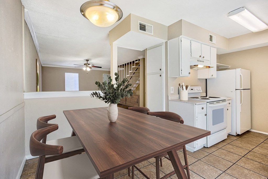 A kitchen with a table and chairs in the foreground and a refrigerator, microwave, and oven in the background.