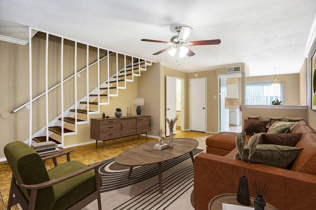 A living room with a brown couch, a green chair, and a staircase with white railings.
