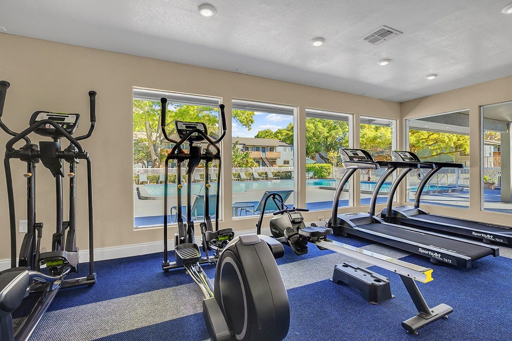 A gym with a view of a pool and trees outside the window.