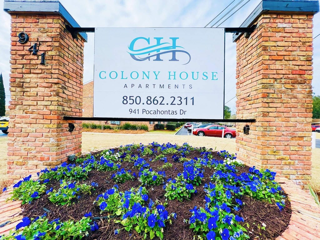 A sign for Colony House Apartments is displayed in front of a flower bed.