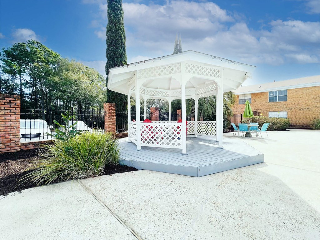A white gazebo with a lattice design is surrounded by a white fence and a brick wall.