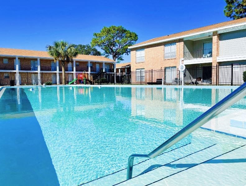 A swimming pool in front of a brick building with a tree in the background.