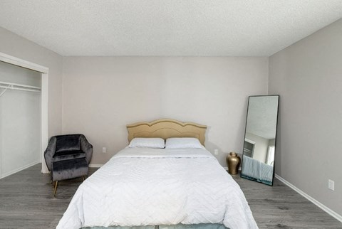 A bedroom with a large bed, a chair, and a mirror.