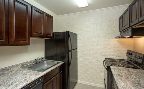 A kitchen with a black refrigerator and a white brick wall.