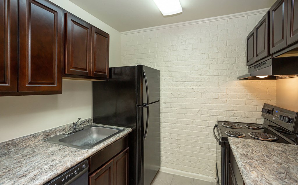 A kitchen with a black refrigerator and a white brick wall.