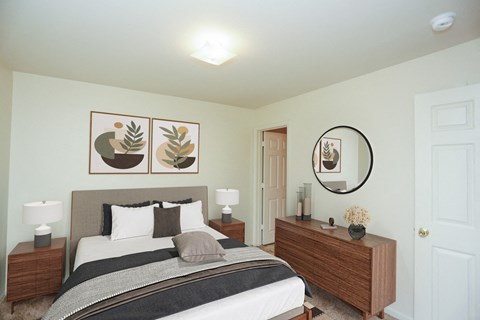 A bedroom with a bed, nightstand, and a mirror with a plant on it.