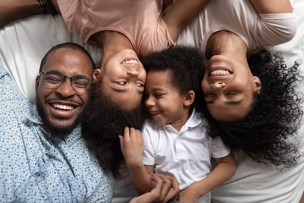 A family of four is lying down together, smiling and enjoying each other's company.