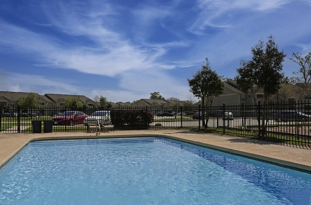 A swimming pool surrounded by a black fence with a red car parked behind it.