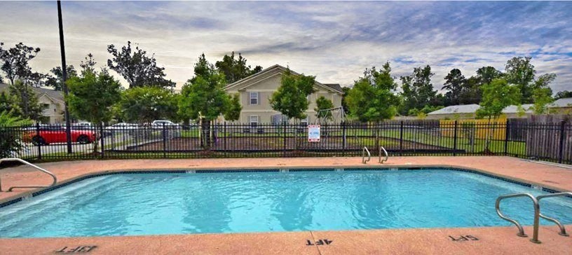 A pool surrounded by a black fence with a house in the background.