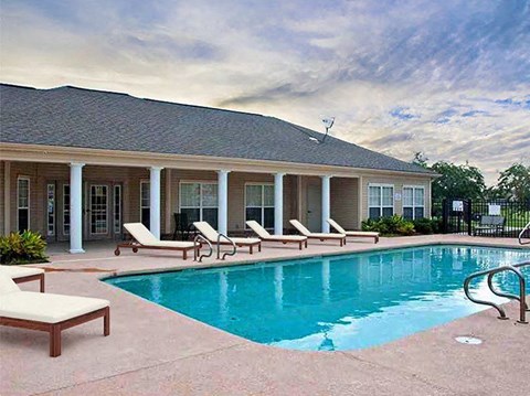 A pool area with sun loungers and a house in the background.