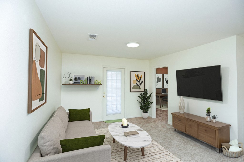 A living room with a grey couch, a coffee table, a plant, and a television.