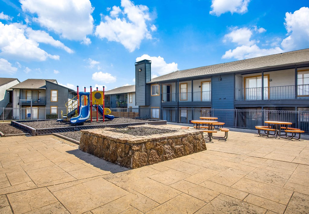 A playground area with a slide, swings, and picnic tables in front of a building.