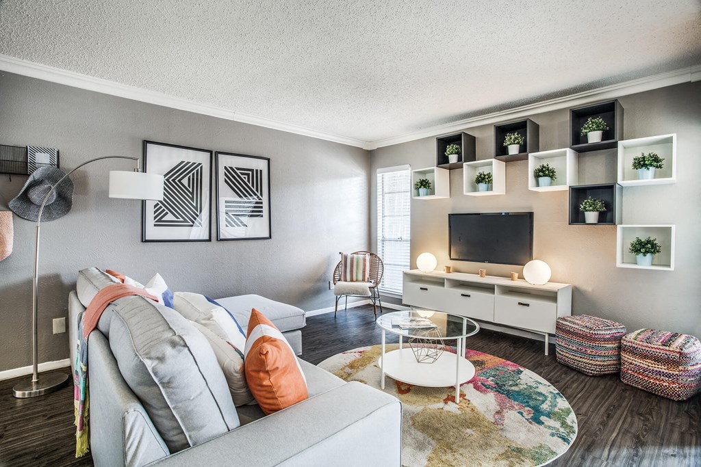 A living room with a grey couch, a white coffee table, and a white TV stand with plants on top.