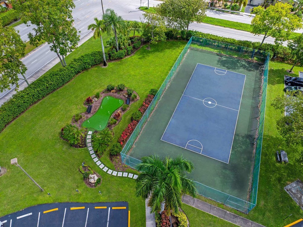 A tennis court surrounded by a green fence and a garden.