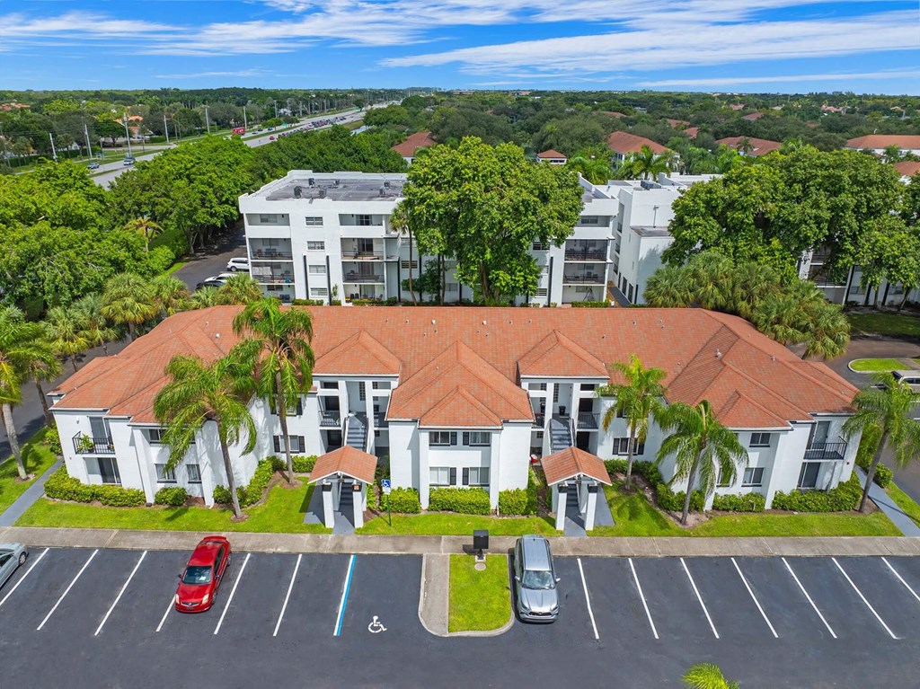 A large white building with a red roof is surrounded by trees and has a parking lot in front.