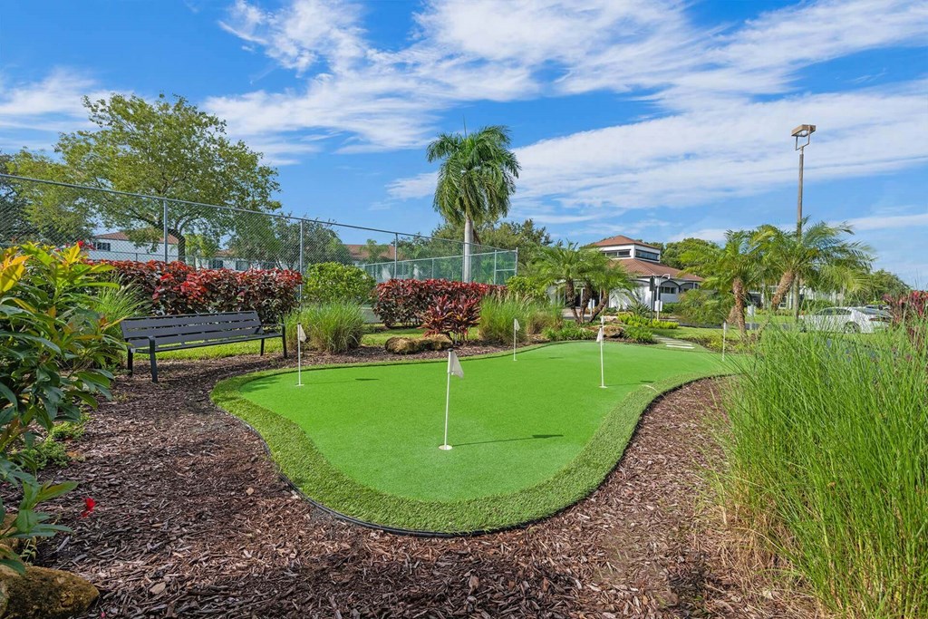 A small putting green is surrounded by shrubbery and trees.