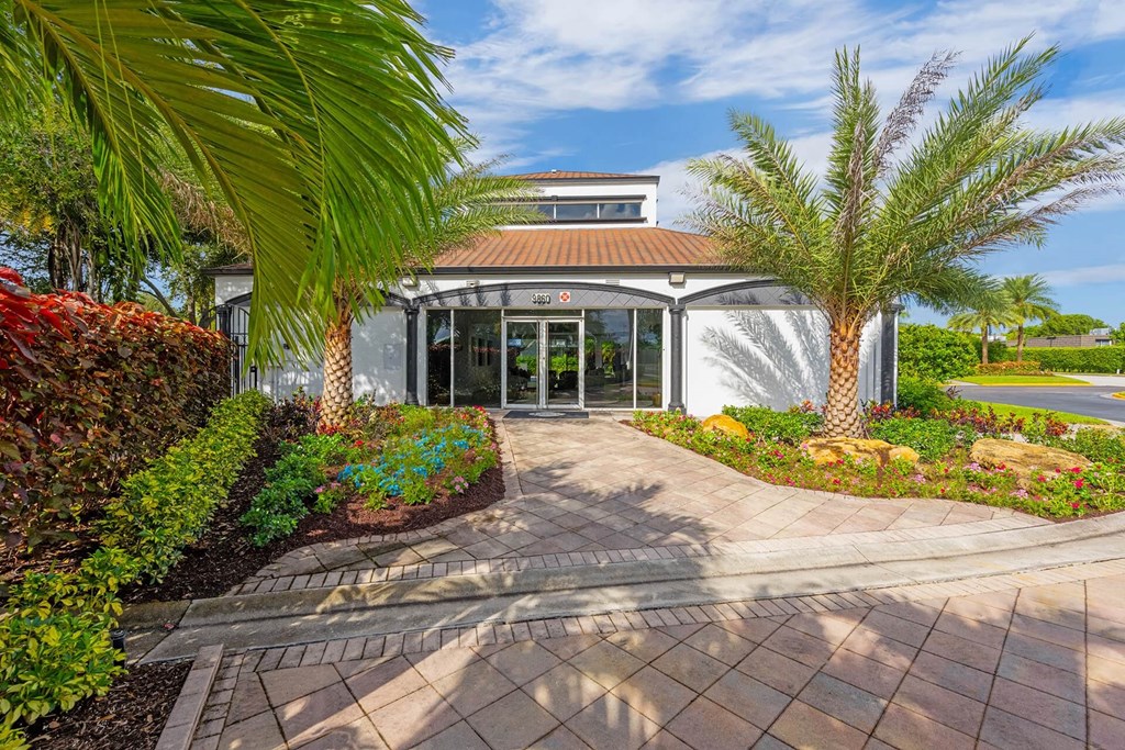 A building with a red roof and glass doors is surrounded by a garden with a brick pathway leading to it.